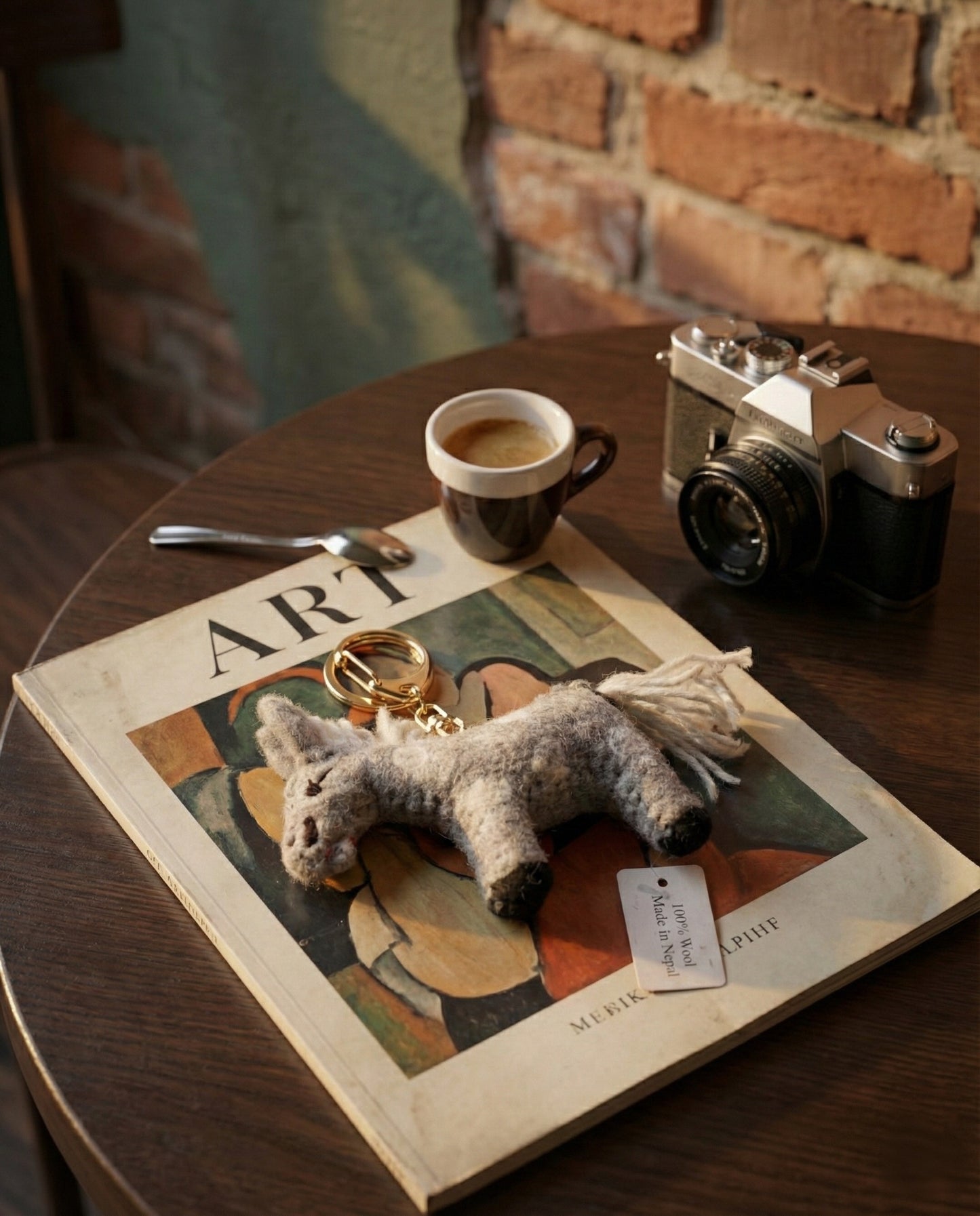 Grey felt donkey keychain with beaded strap on art magazine next to vintage camera