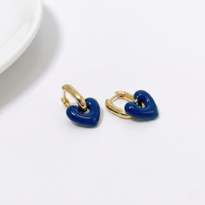 Navy blue puffy heart earrings hanging from gold huggie hoops shown on white background