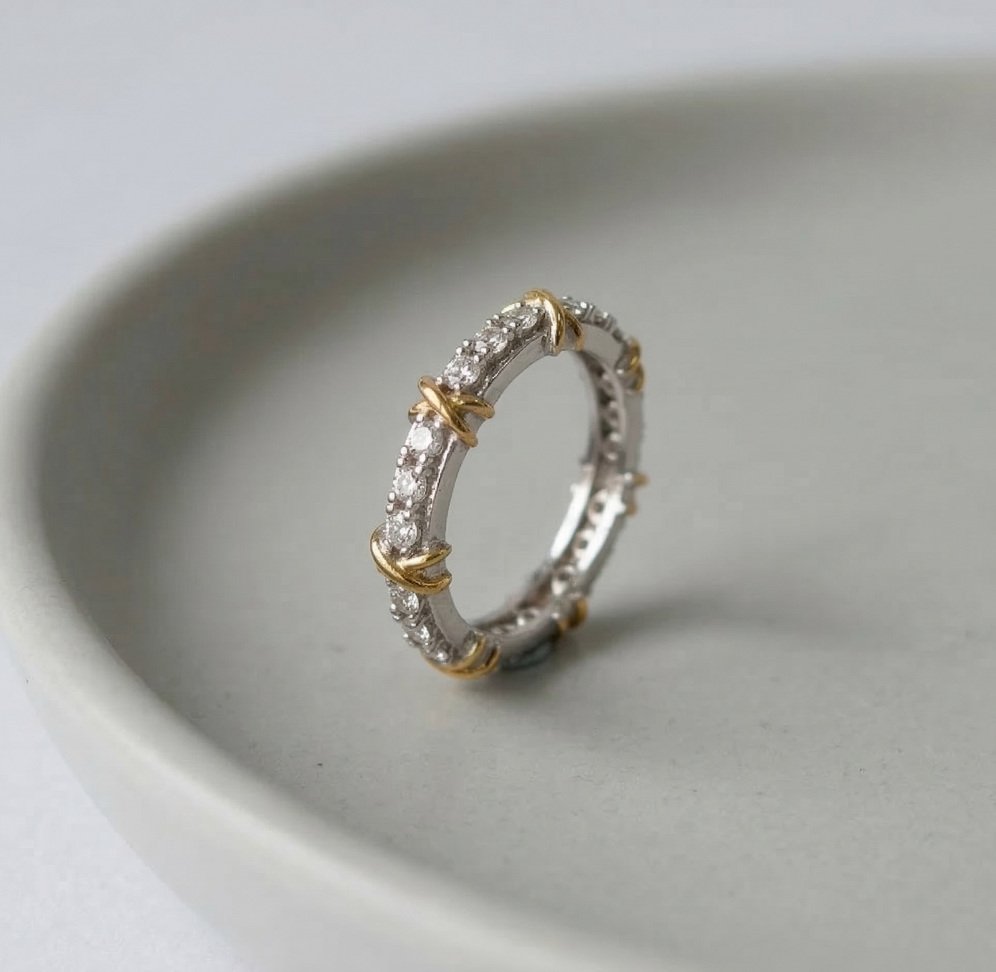 Front-facing view of the 925 sterling silver two-tone eternity ring inside a ceramic dish, showcasing the full pavé cubic zirconia band and rhythmic gold X-cross accents