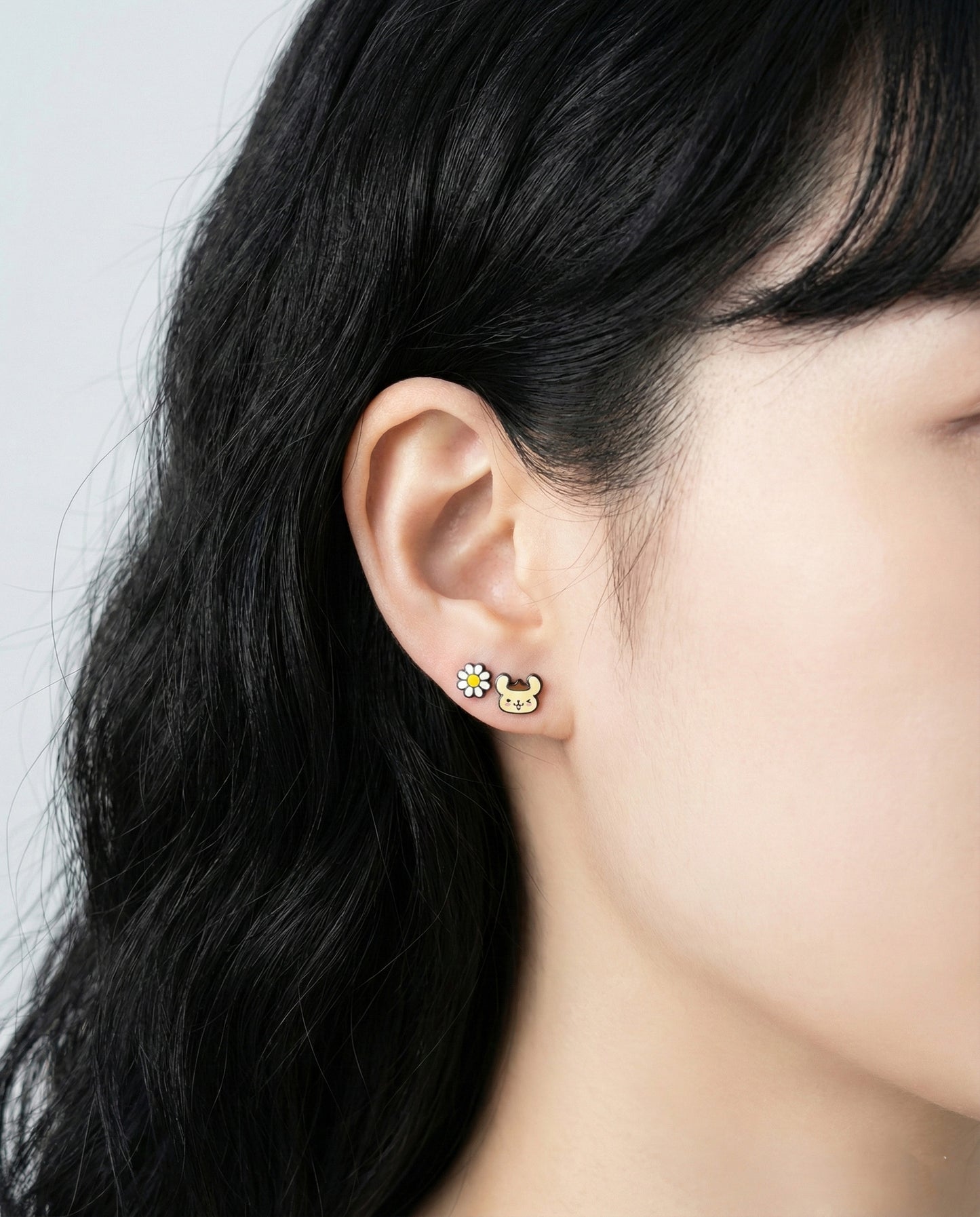Close-up of Pompompurin character earrings with flower and bee enamel studs on ear"