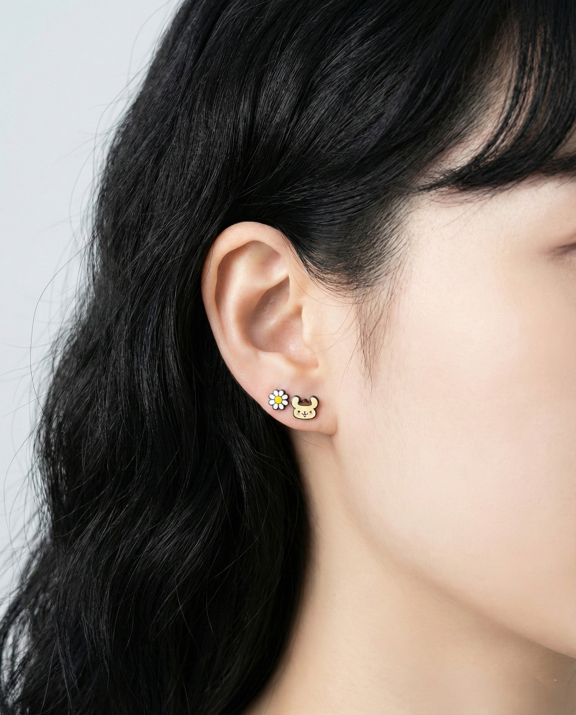 Close-up of Pompompurin character earrings with flower and bee enamel studs on ear"
