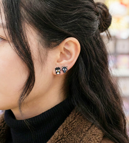 Woman wearing small black cartoon character stud earrings, side profile showing penguin and cat design on earlobe