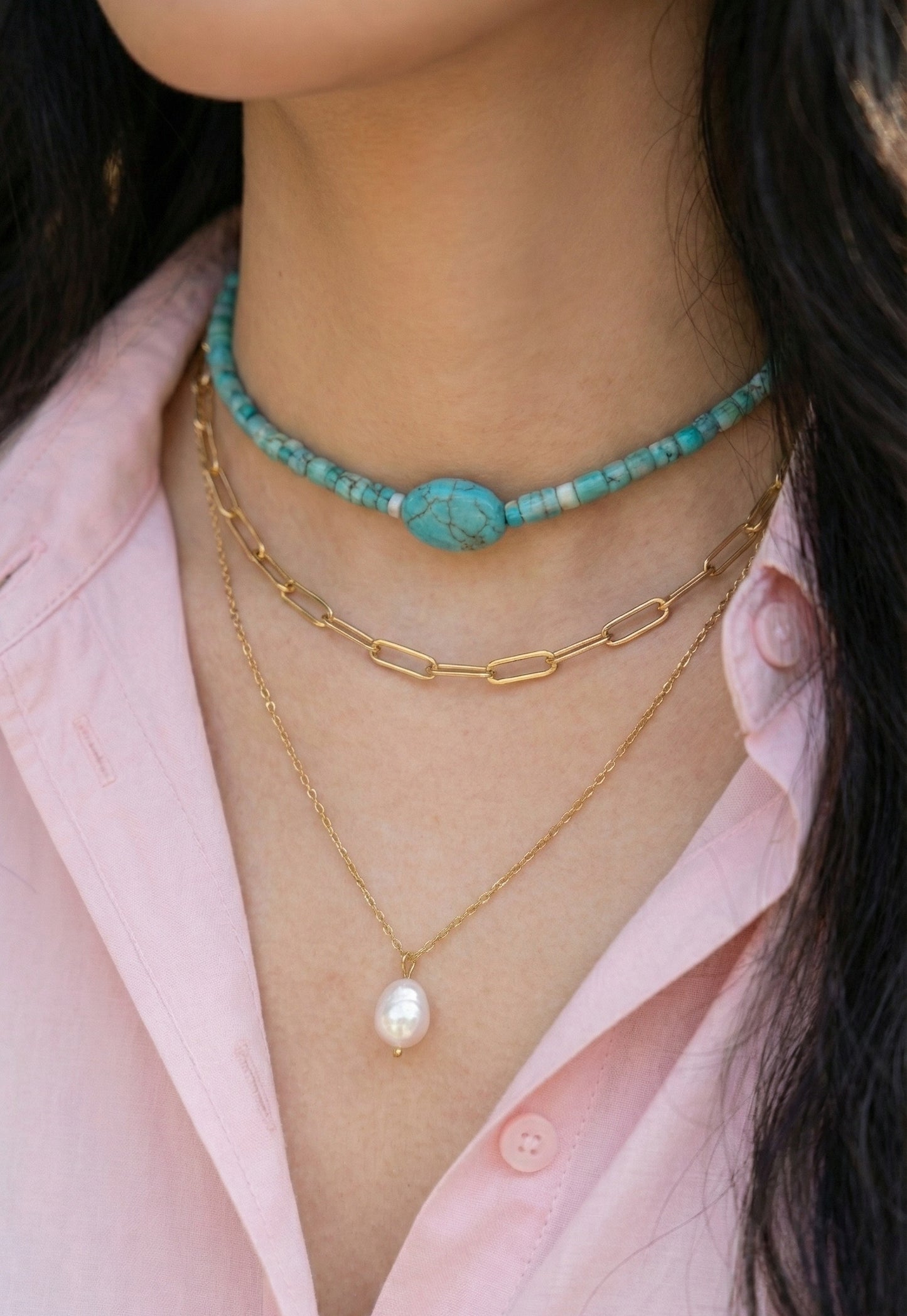 Woman wearing turquoise shell bead choker layered with gold chain necklaces"