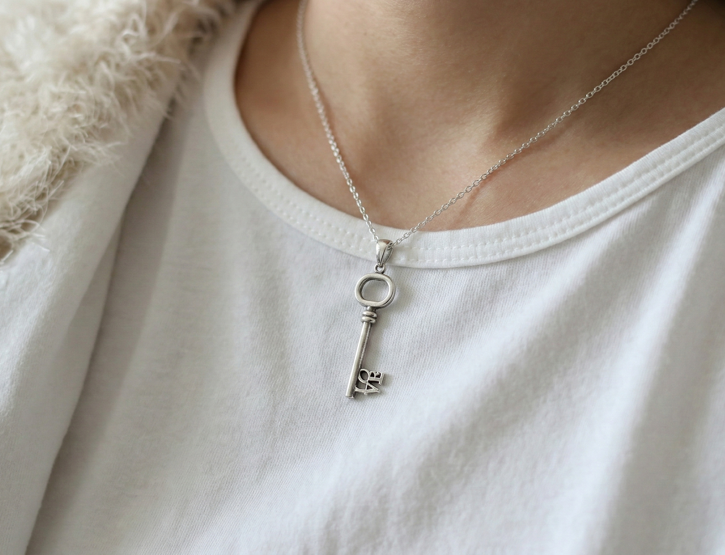  Model wearing the LOVE key necklace over a white t-shirt and fuzzy cream cardigan for a cozy look.