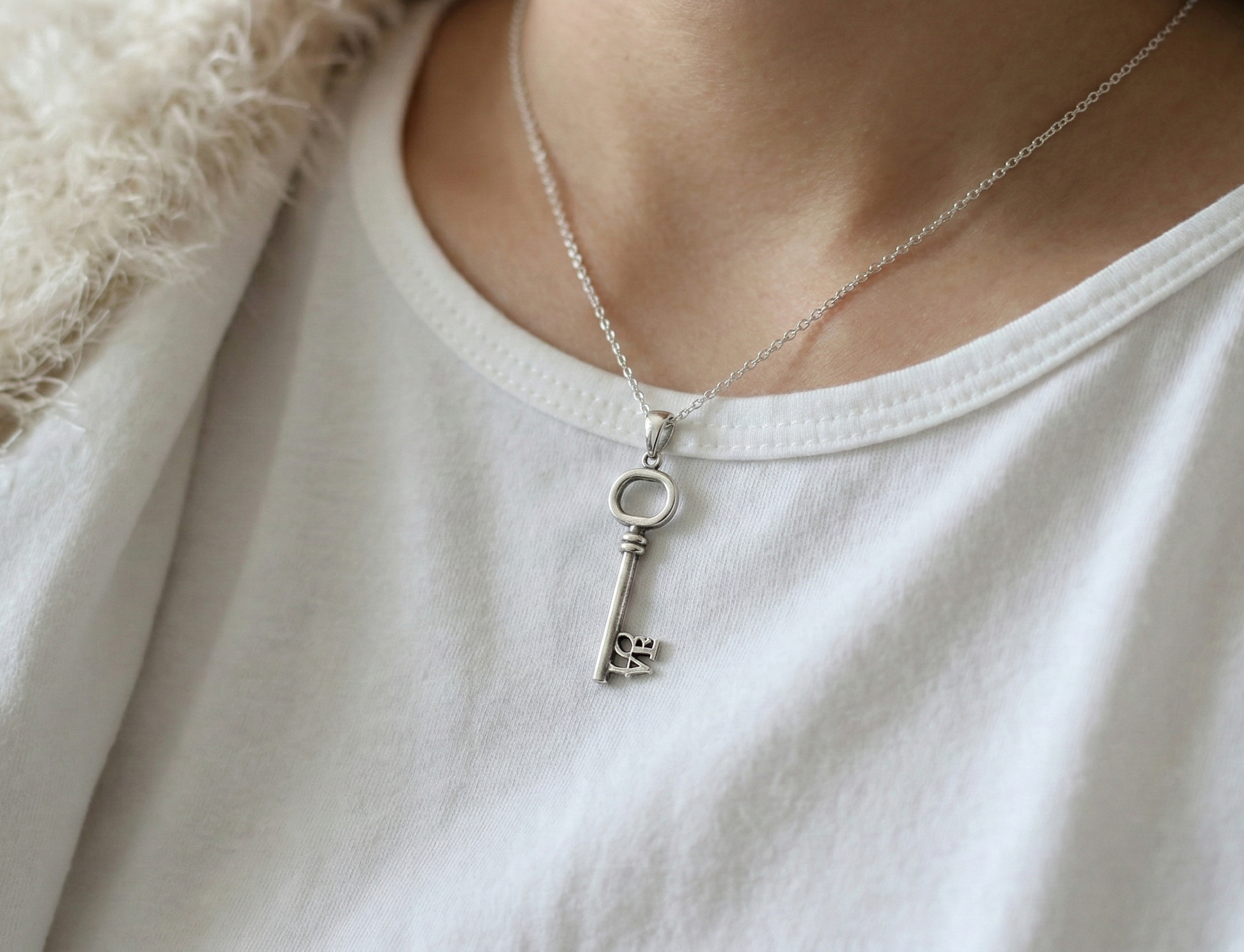 Model wearing the LOVE key necklace over a white t-shirt and fuzzy cream cardigan for a cozy look.