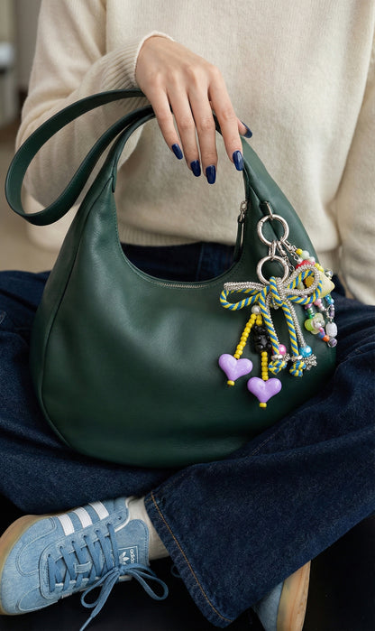 Close-up of pink and mint pastel rope bow bag charm on green hobo bag with purple heart charms