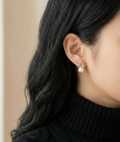 Silver bow pearl stud earrings worn outdoors in natural light, Balletcore aesthetic