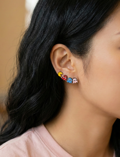 Close-up of woman's ear with full set of four Pac-Man and ghost enamel studs layered — Pac-Man followed by red, blue, and pink ghost in a row
