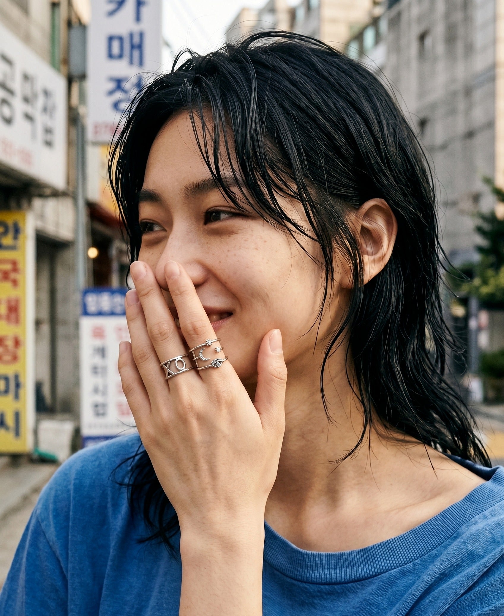 Korean street snap model wearing silver evil eye layered ring stacked with XO chunky silver ring, urban kitsch mix-match ring inspo.