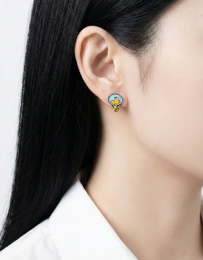 Close-up of a woman wearing a silver post earring featuring Woodstock in a blue space helmet, facing right.
