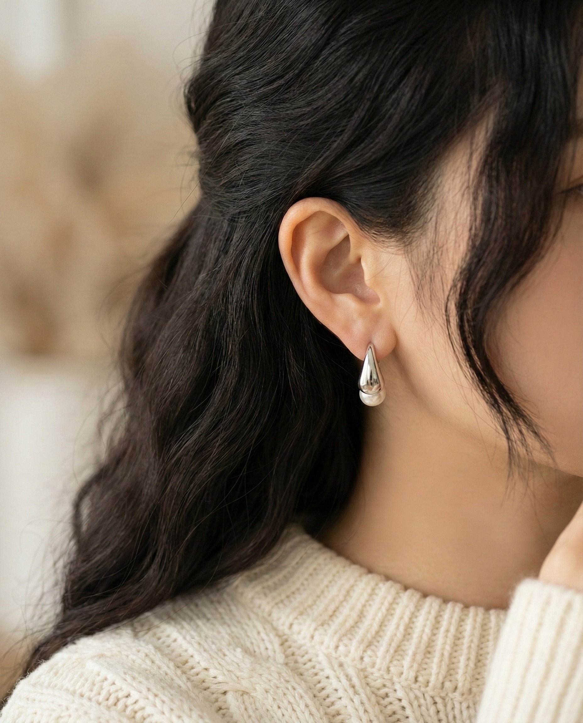 Side view of model wearing silver pearl huggie hoop earrings with cream sweater