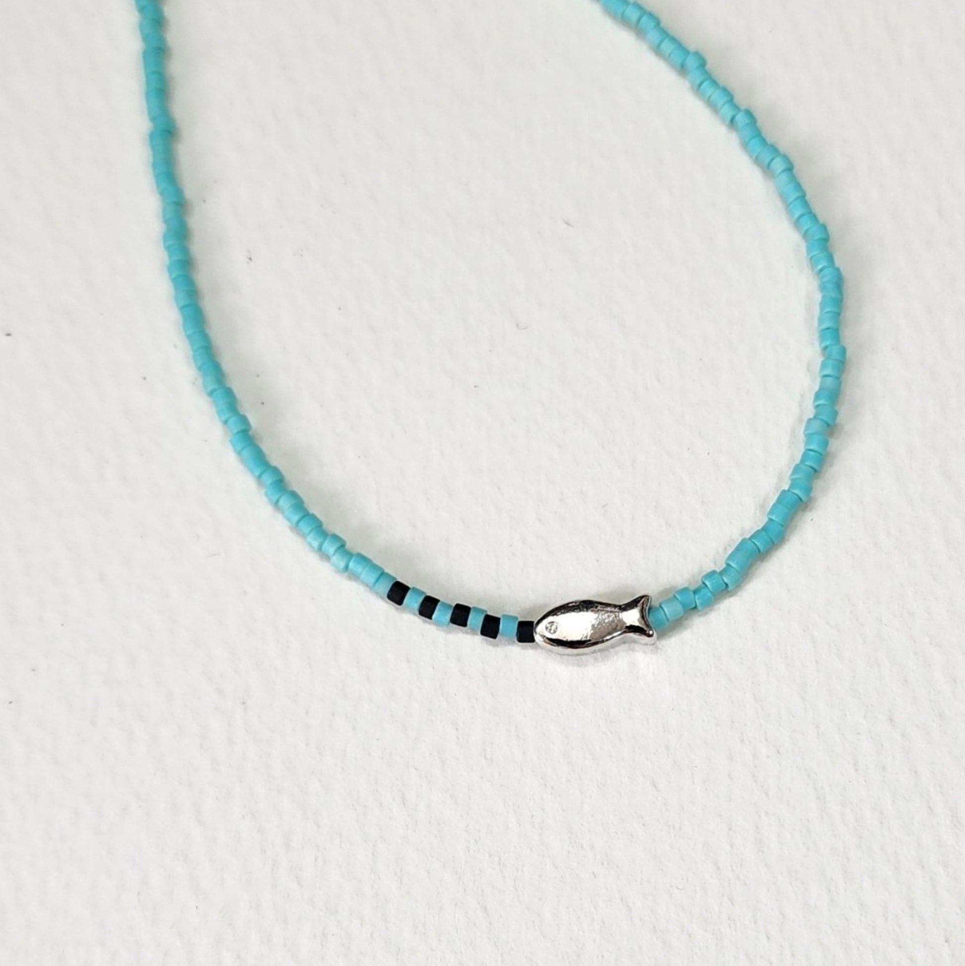  Close-up detail of mint turquoise seed bead necklace with tiny silver fish charm and black accent beads