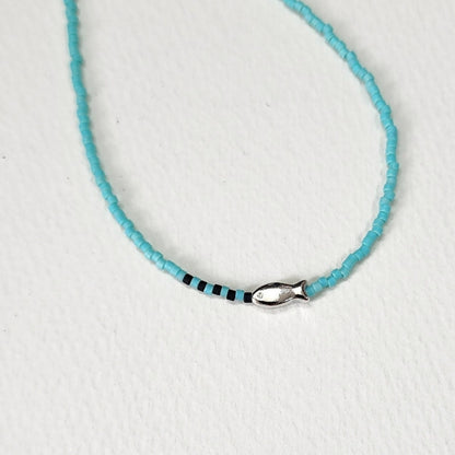  Close-up detail of mint turquoise seed bead necklace with tiny silver fish charm and black accent beads