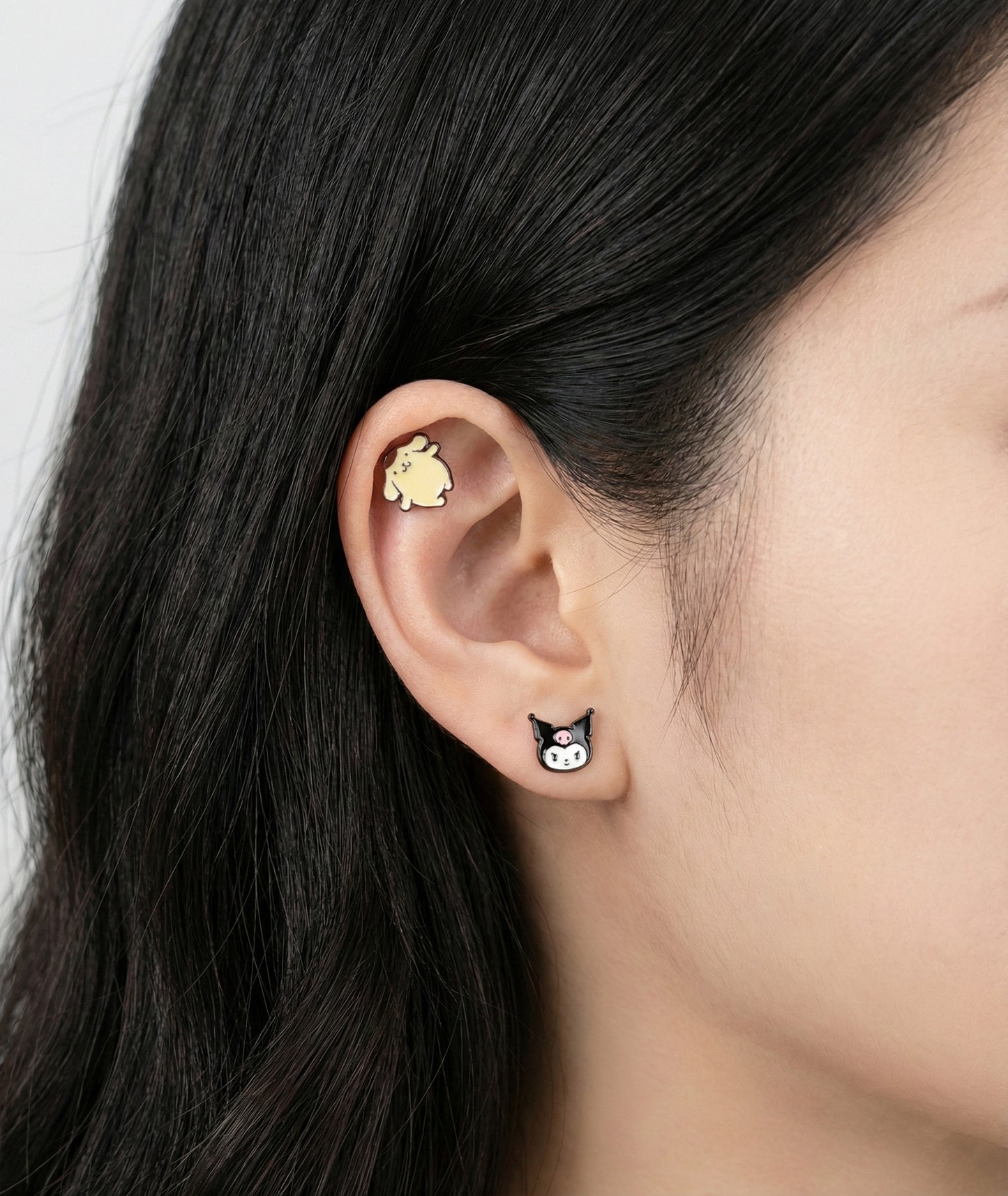 Model ear showing Pompompurin and Kuromi character piercings on outer conch and lobe placement