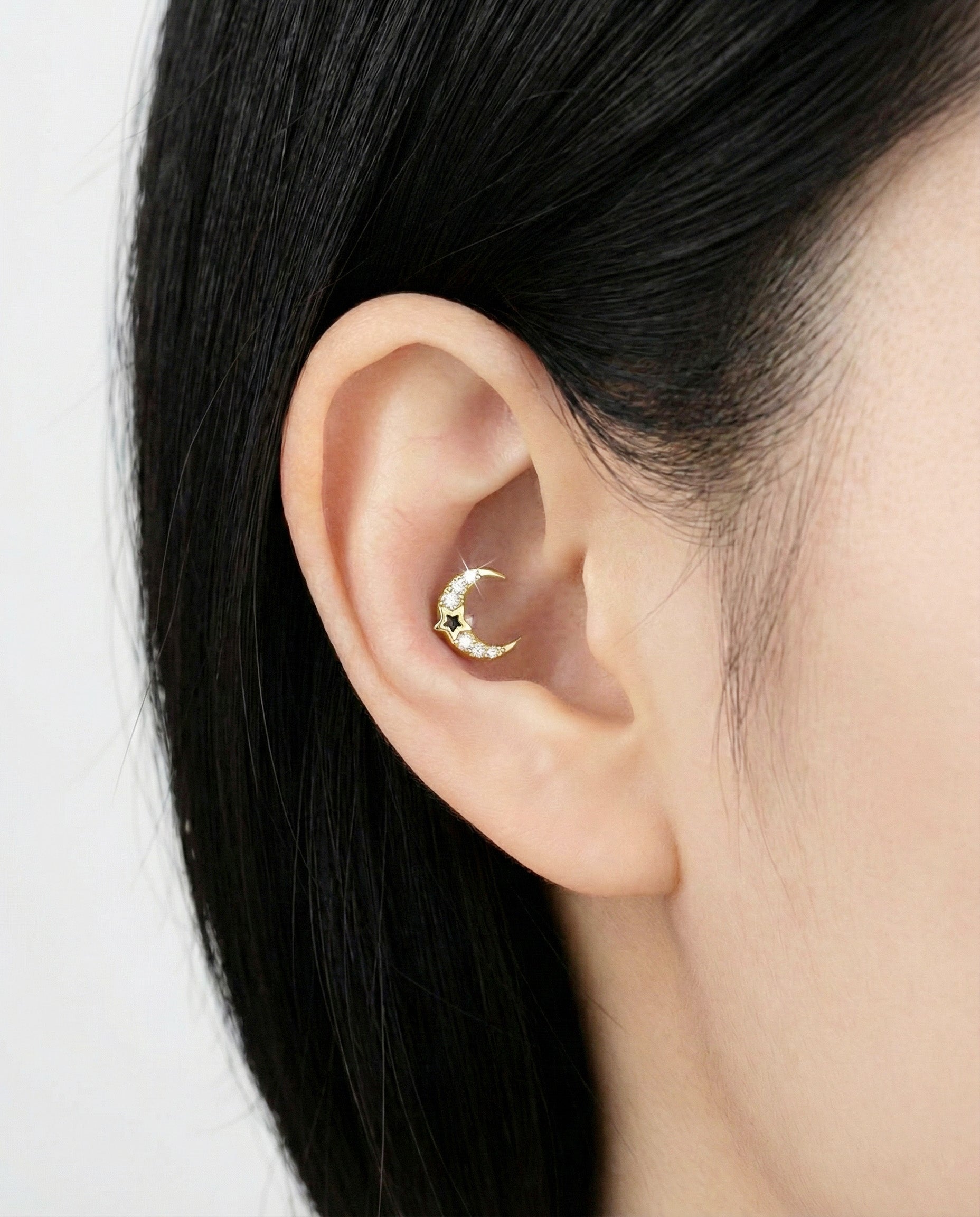 Gold crescent moon earring with crystal accents and a black star detail, styled in the inner ear.