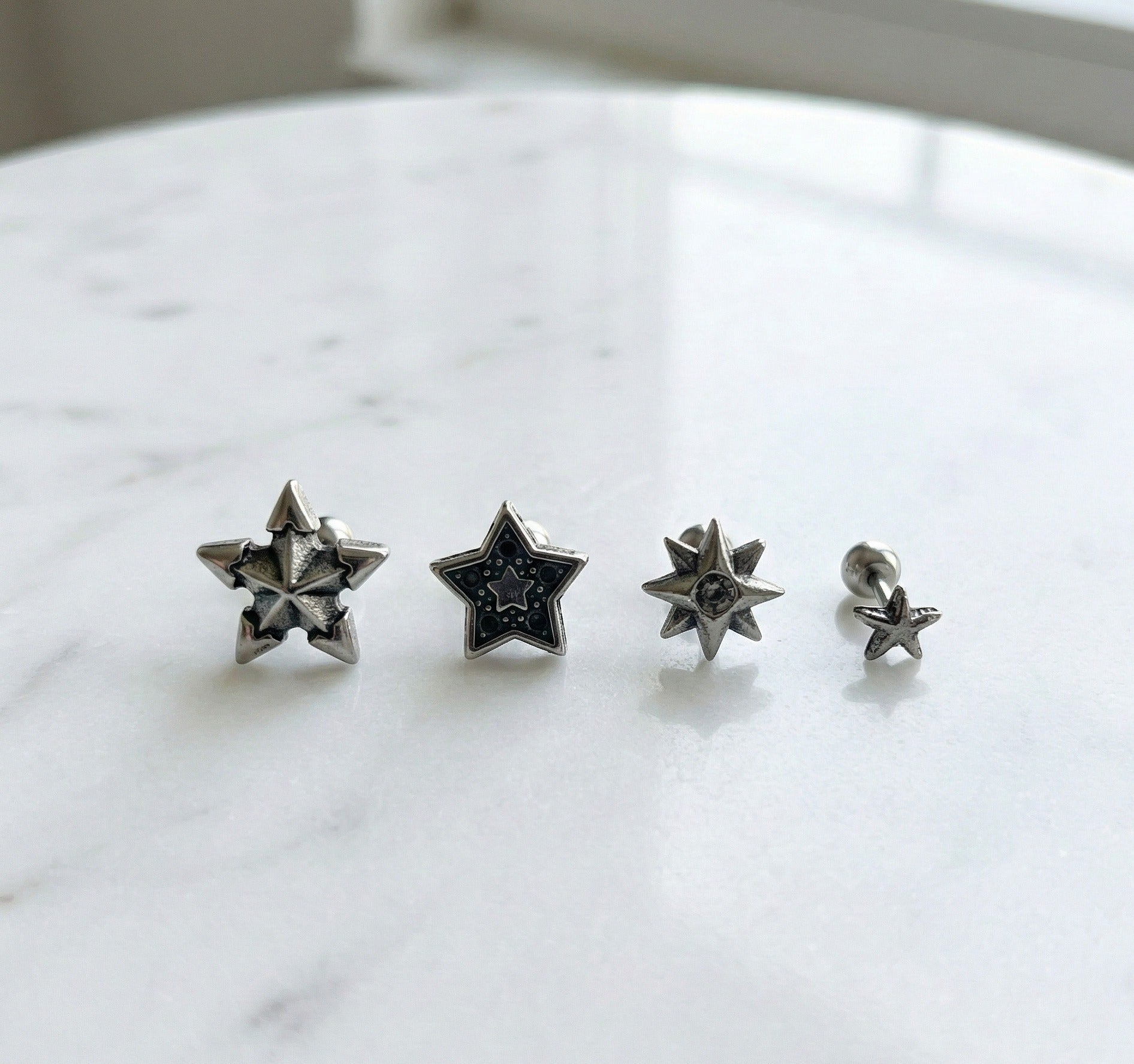 Four vintage silver star barbell piercings arranged by size on white marble surface