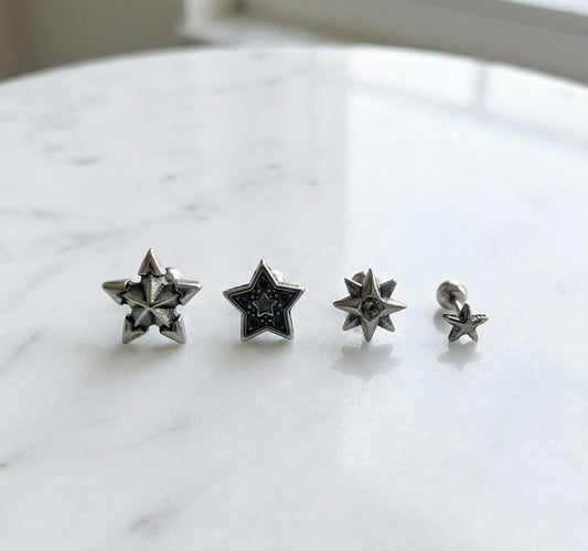 Four vintage silver star barbell piercings arranged by size on white marble surface