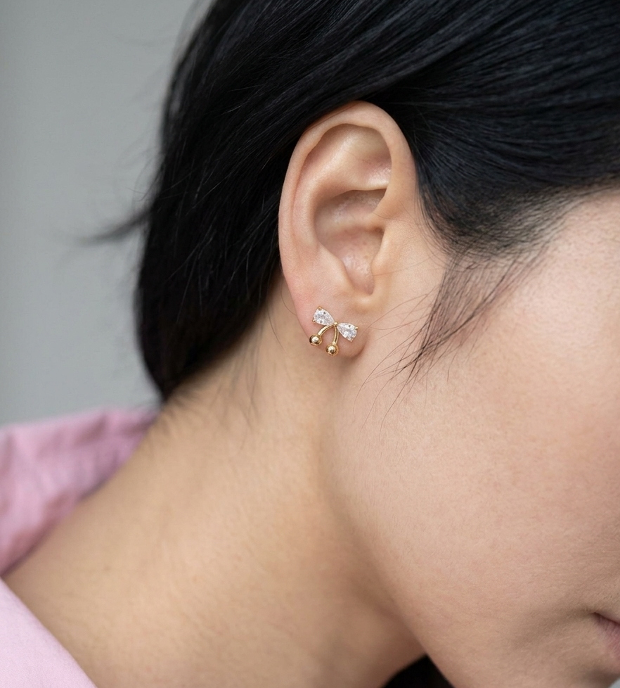 Close-up of gold CZ bow cherry stud earrings propped against a rounded ceramic object, highlighting pear-cut cubic zirconia setting and polished ball drops