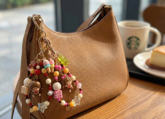 Vintage Monchhichi keychain with yellow gingham beads hanging from brown leather hobo bag with colorful beaded loop and clear star charm