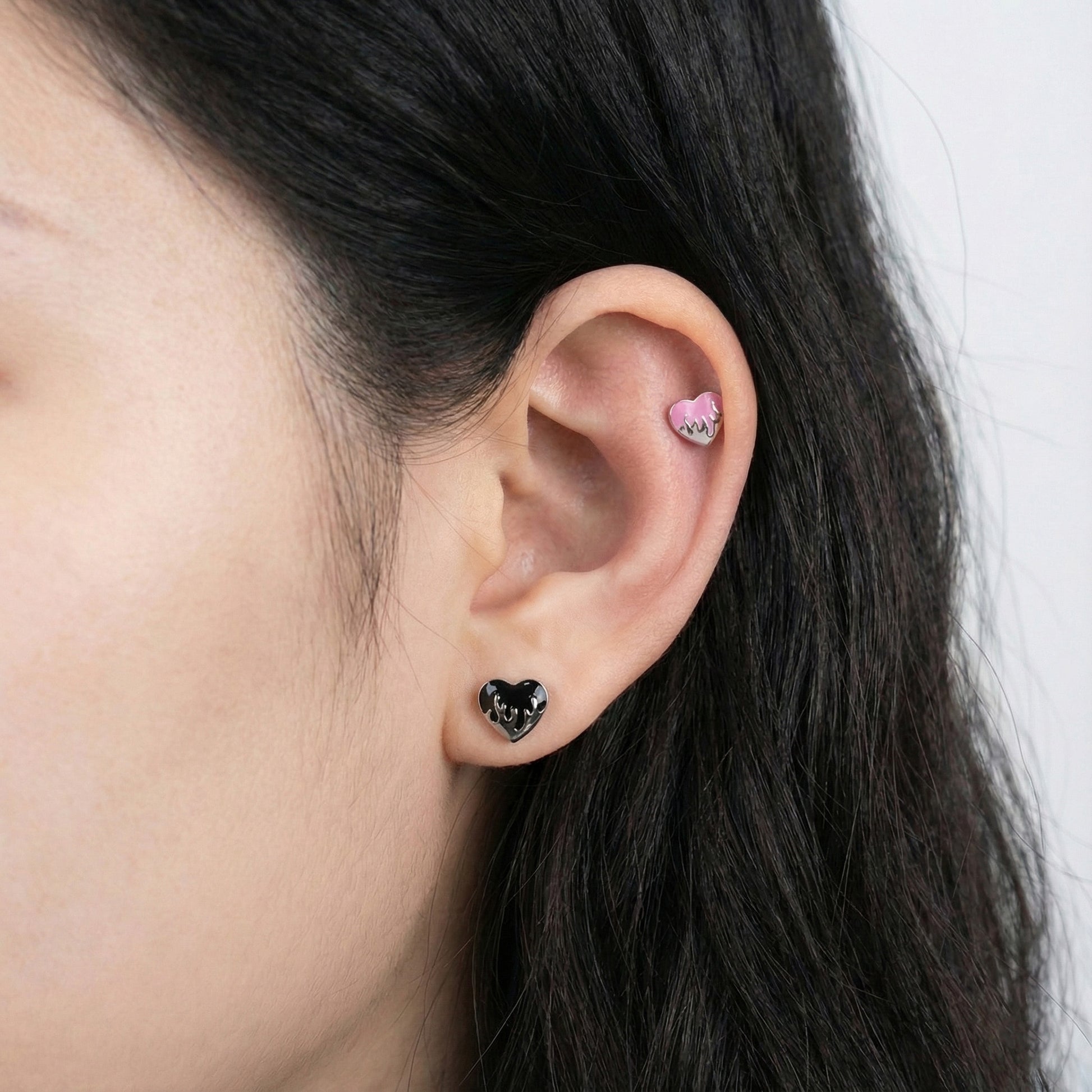 Black melting heart stud on lobe and pink on inner conch showing versatile cartilage piercing placement