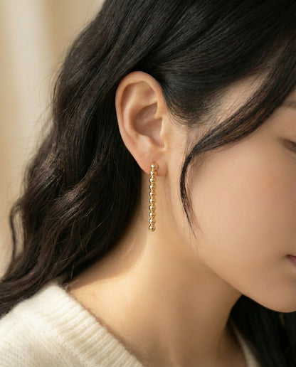 Woman wearing gold ball bar drop earrings with cream knit sweater - side profile