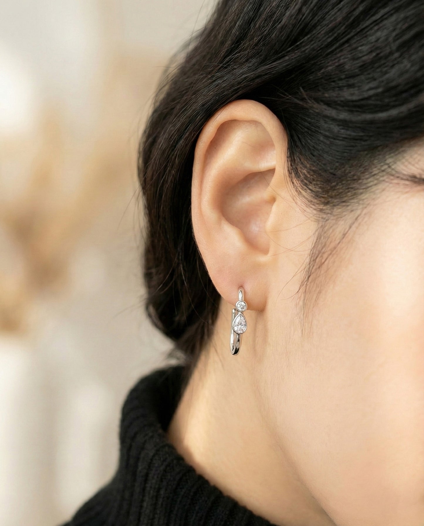 Side view of silver bezel-set pear-cut cubic zirconia U-hoop earrings on model