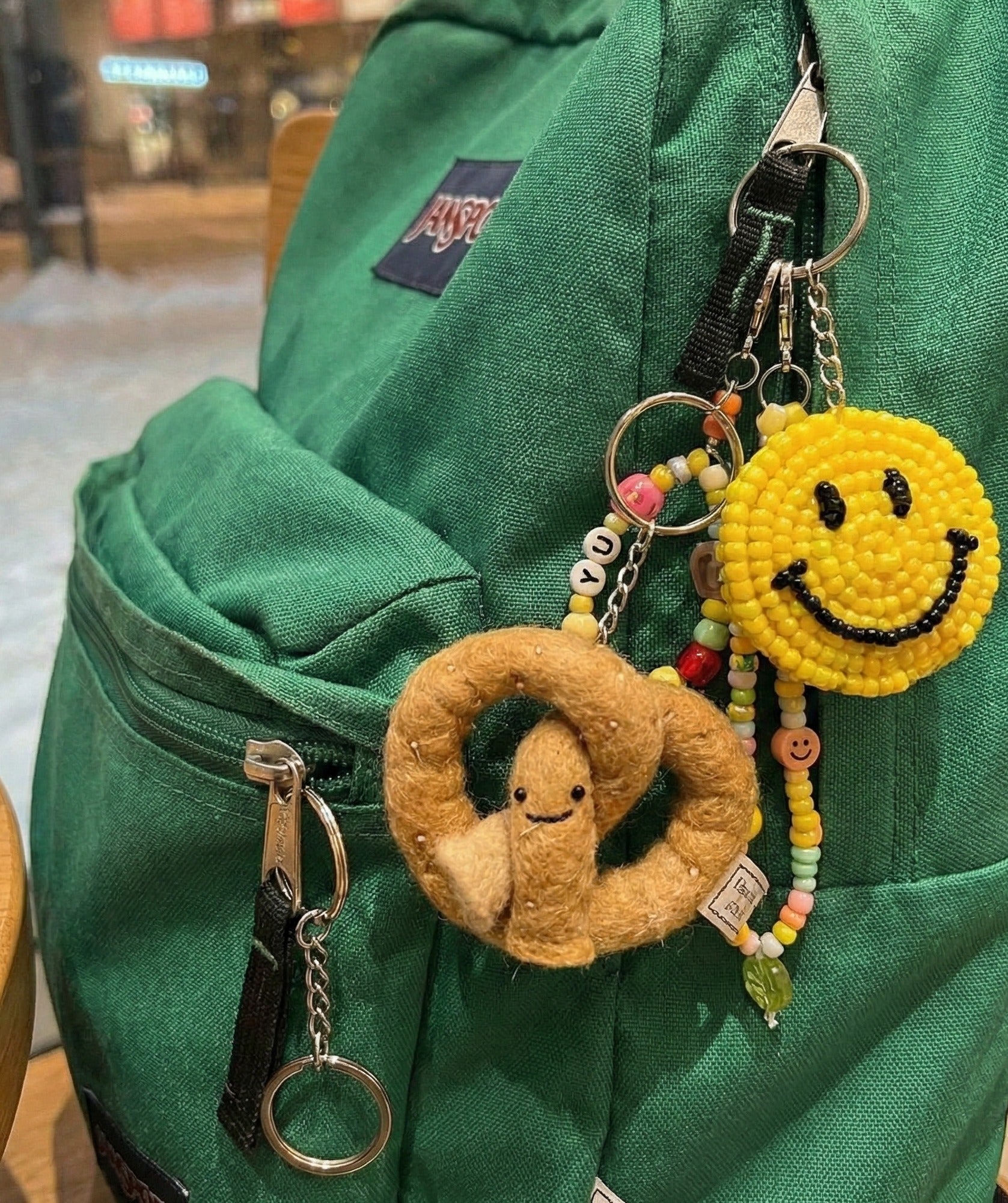 Cute felt pretzel keychain attached to green Jansport backpack with colorful bead charm