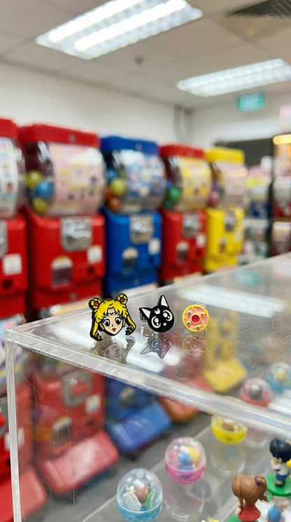 Sailor Moon anime earring set displayed on clear acrylic box with colorful gachapon machines background
