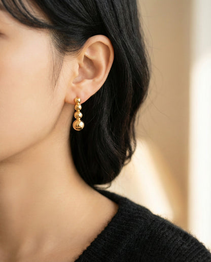 Woman wearing gold graduated ball bar earrings with black turtleneck sweater