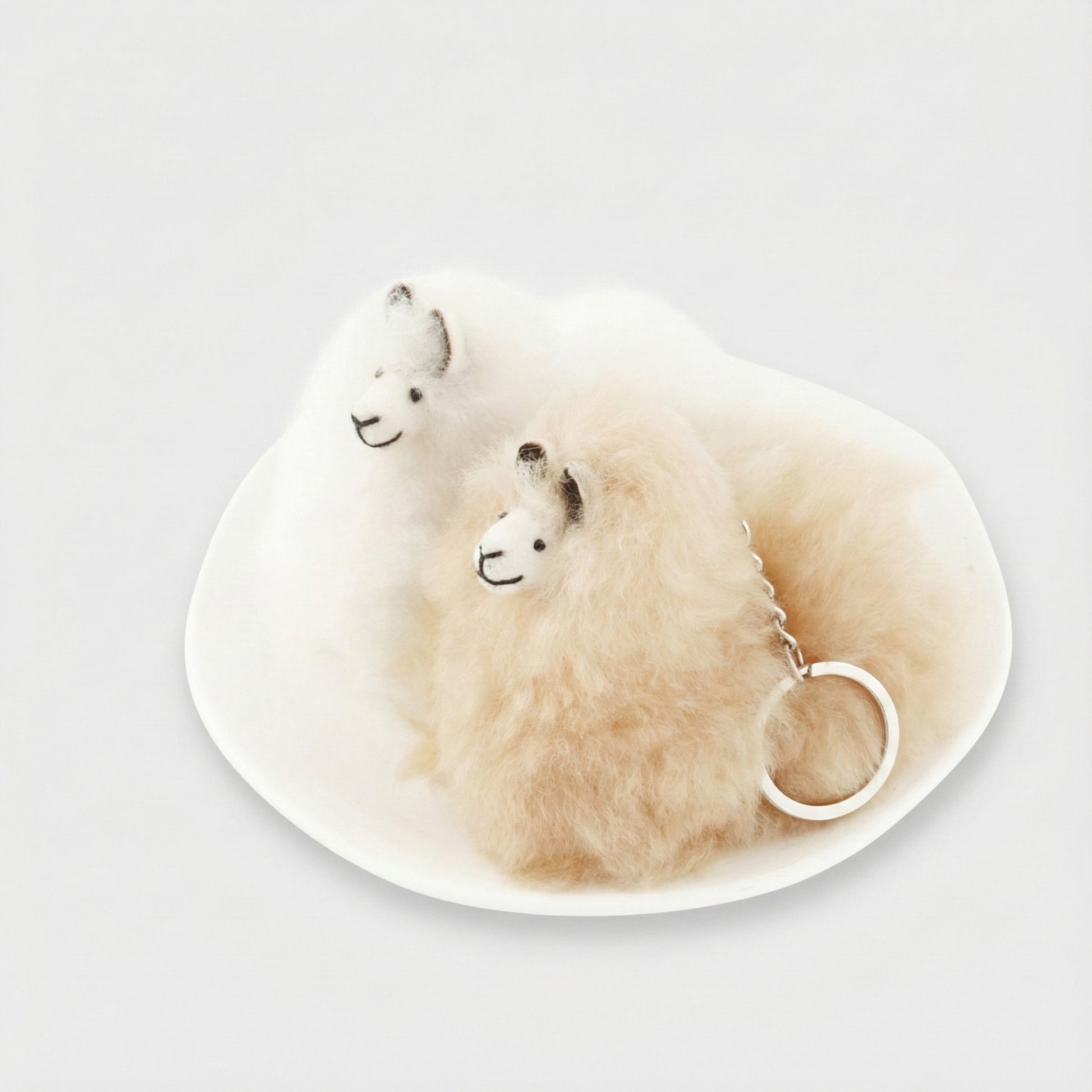 White and beige alpaca keychains on ceramic plate side by side