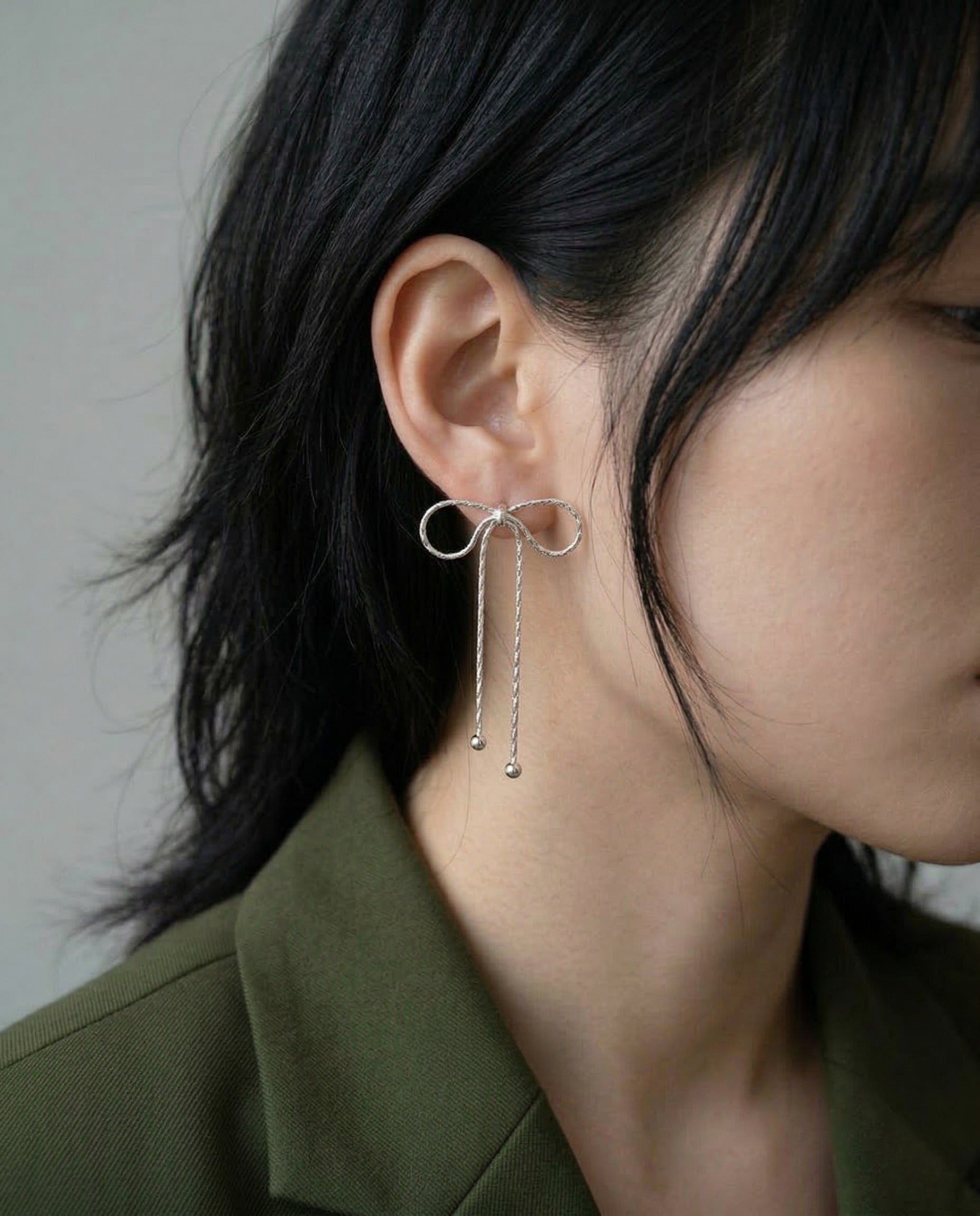 Model wearing silver textured chain bow drop earrings with dark blazer, side profile with hair down, showcasing dainty drop effect