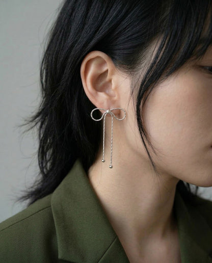 Model wearing silver textured chain bow drop earrings with dark blazer, side profile with hair down, showcasing dainty drop effect