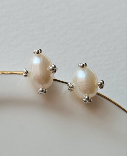 Silver oval pearl stud earrings placed on a minimal white surface.”
