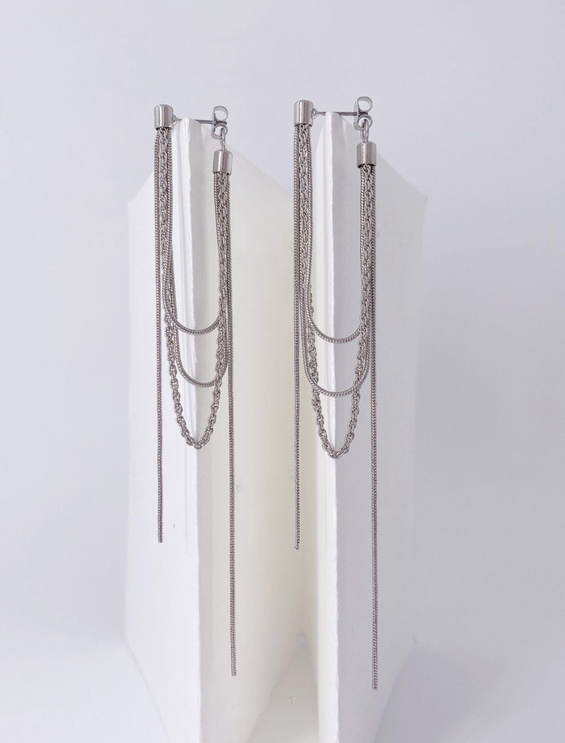 Pair of silver front back drop earrings showing layered chain detail on white stand