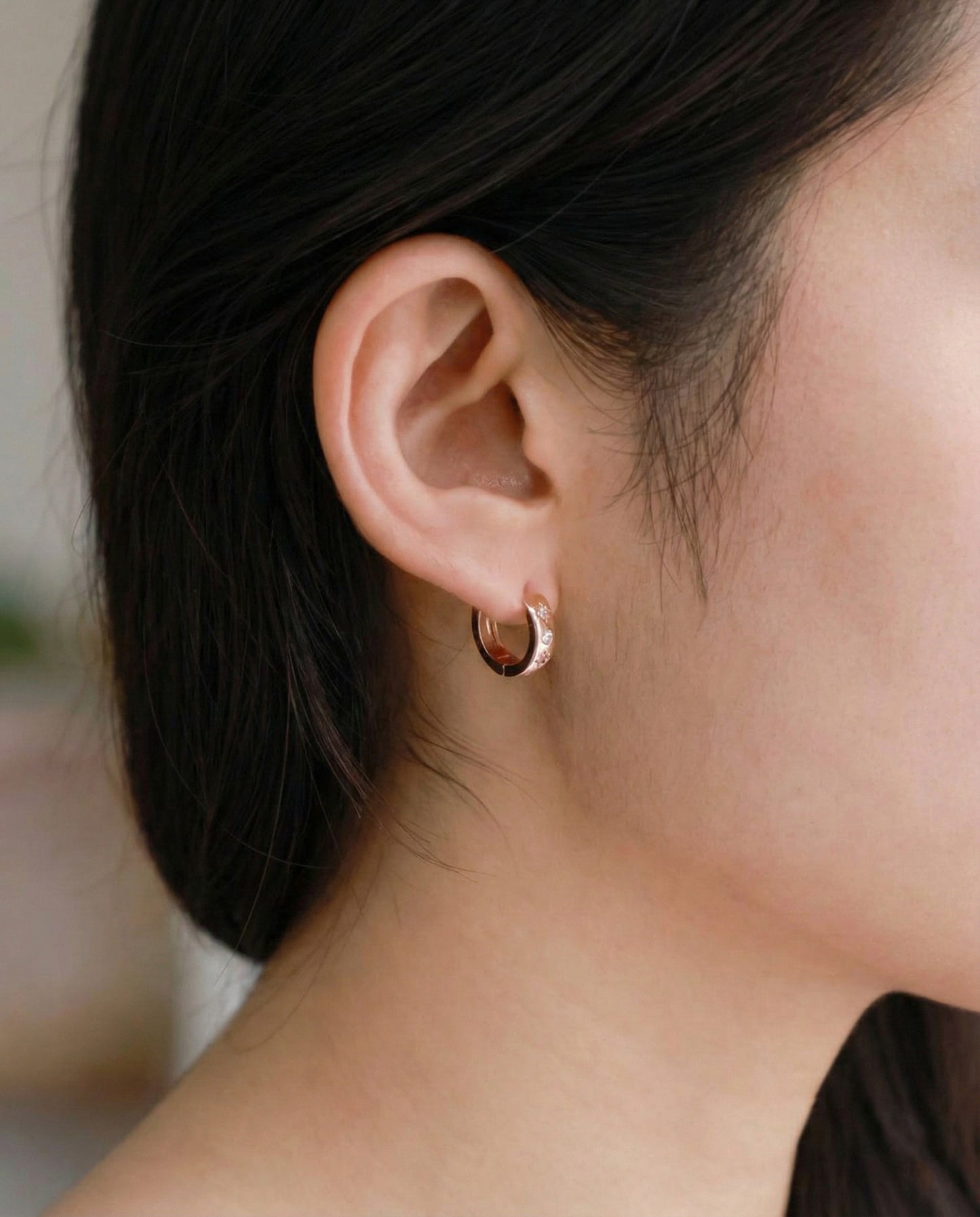 Rose gold hoop earring with sparkly star detail shown on the right ear from a soft profile view.