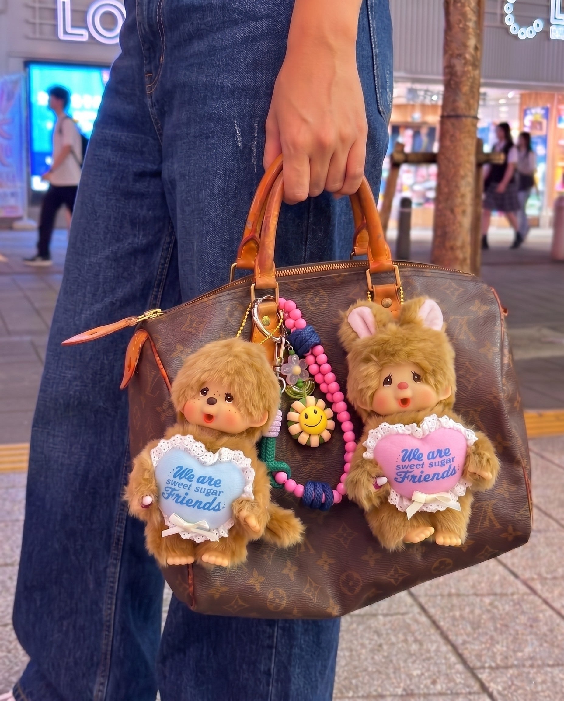 Urban kitsch bag charm look — Monchhichi blue heart classic on Louis Vuitton Damier tote, K-style bag decoration inspo with purple smile bead strap.