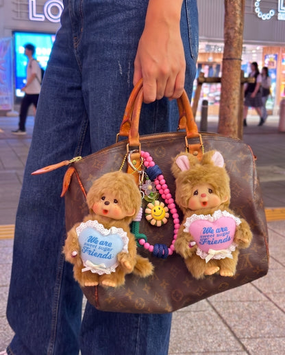 Urban kitsch bag charm look — Monchhichi blue heart classic on Louis Vuitton Damier tote, K-style bag decoration inspo with purple smile bead strap.
