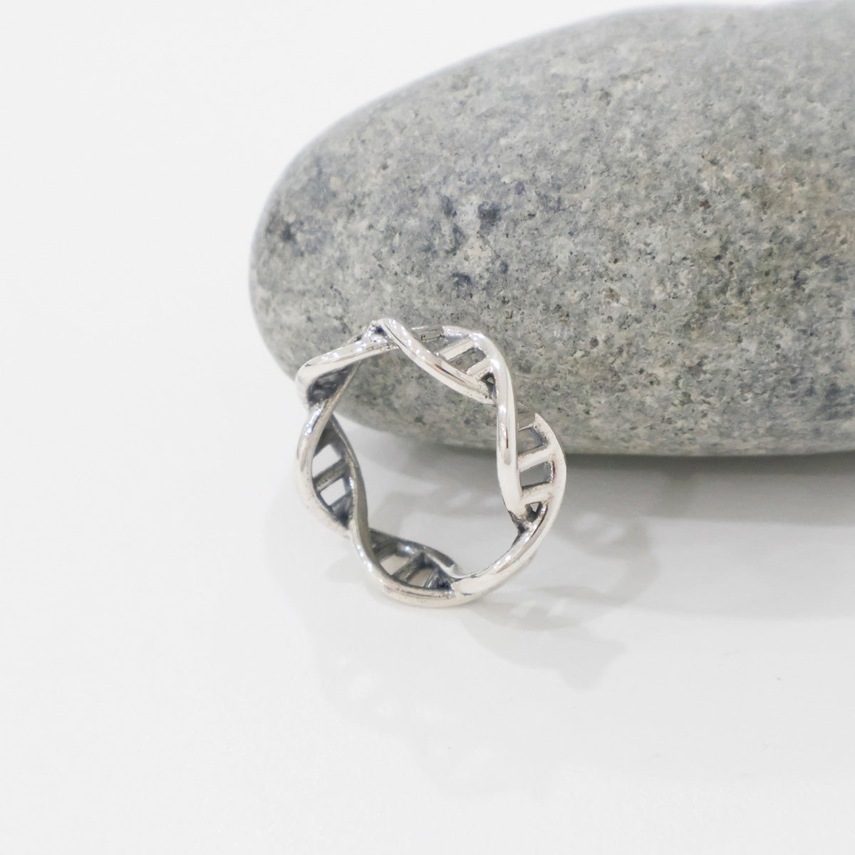 Twisted DNA double-helix silver ring standing upright next to a textured grey stone.