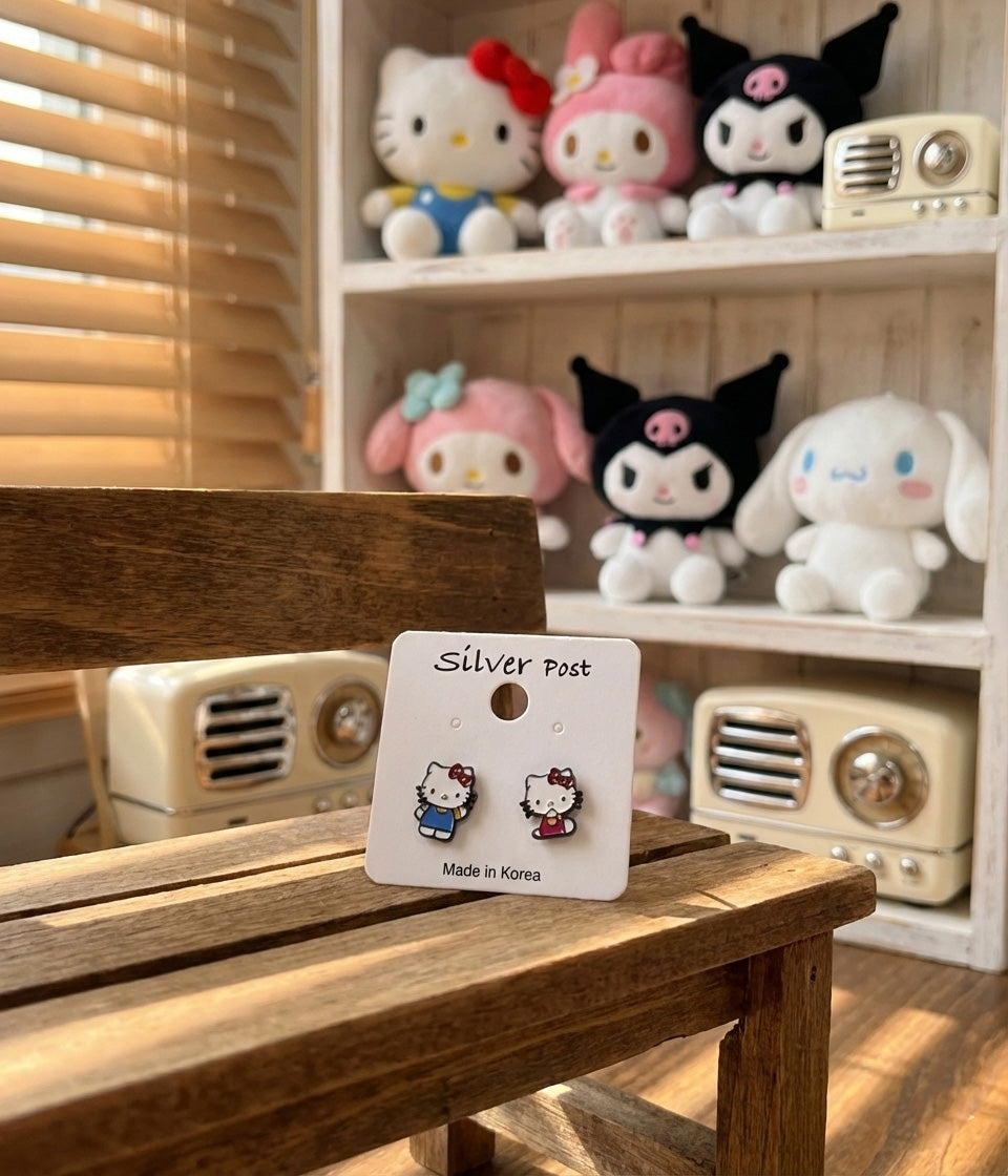Hello Kitty asymmetrical earrings on white card with Sanrio character plushies in background