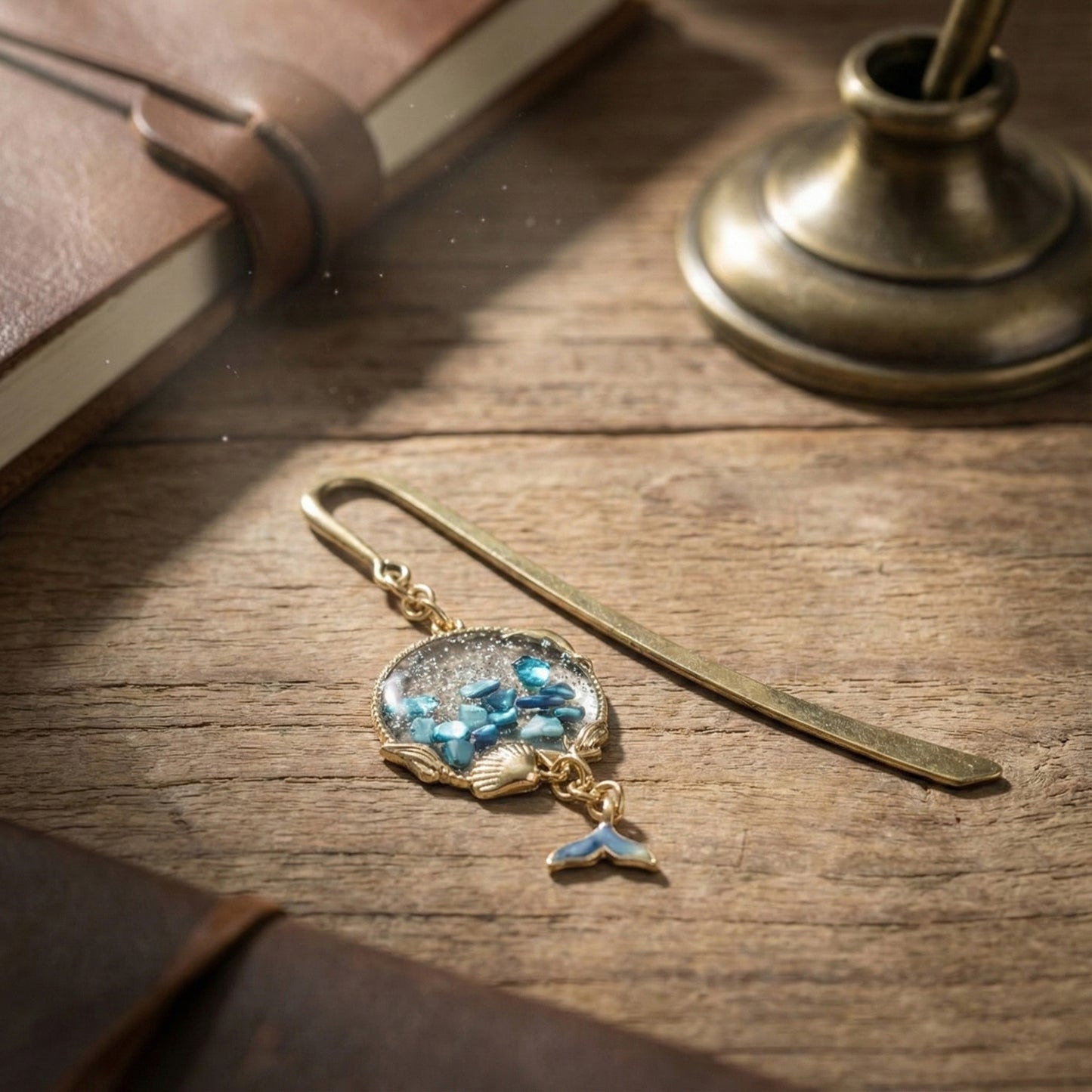 Close-up of gold whale tail bookmark with turquoise resin shell charm on wooden desk