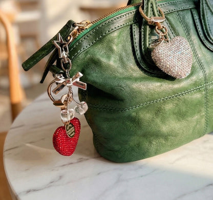 Close-up of green leather handbag with red heart charm and silver accessories