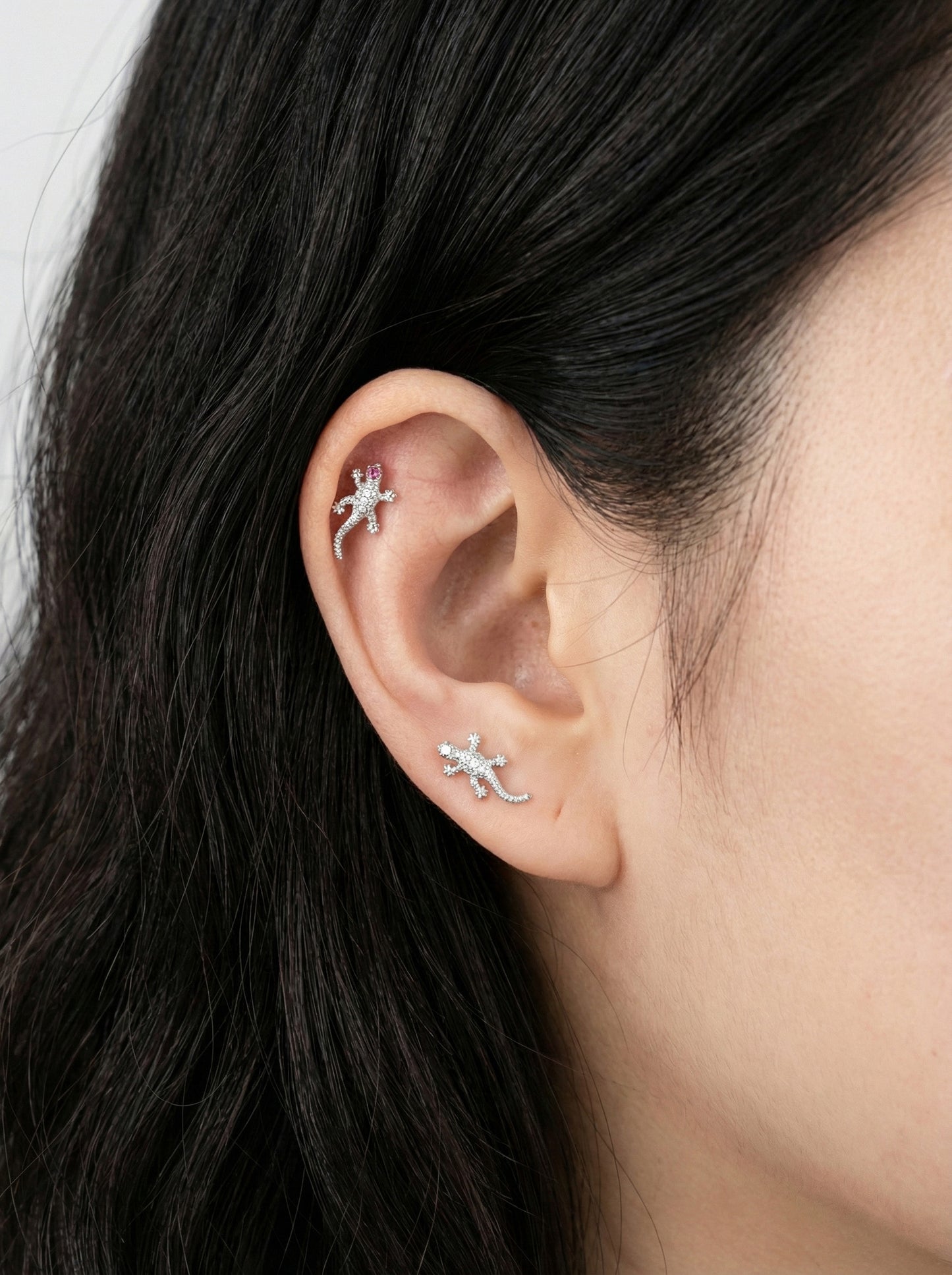 Close-up of an ear with two small lizard-shaped earrings.
