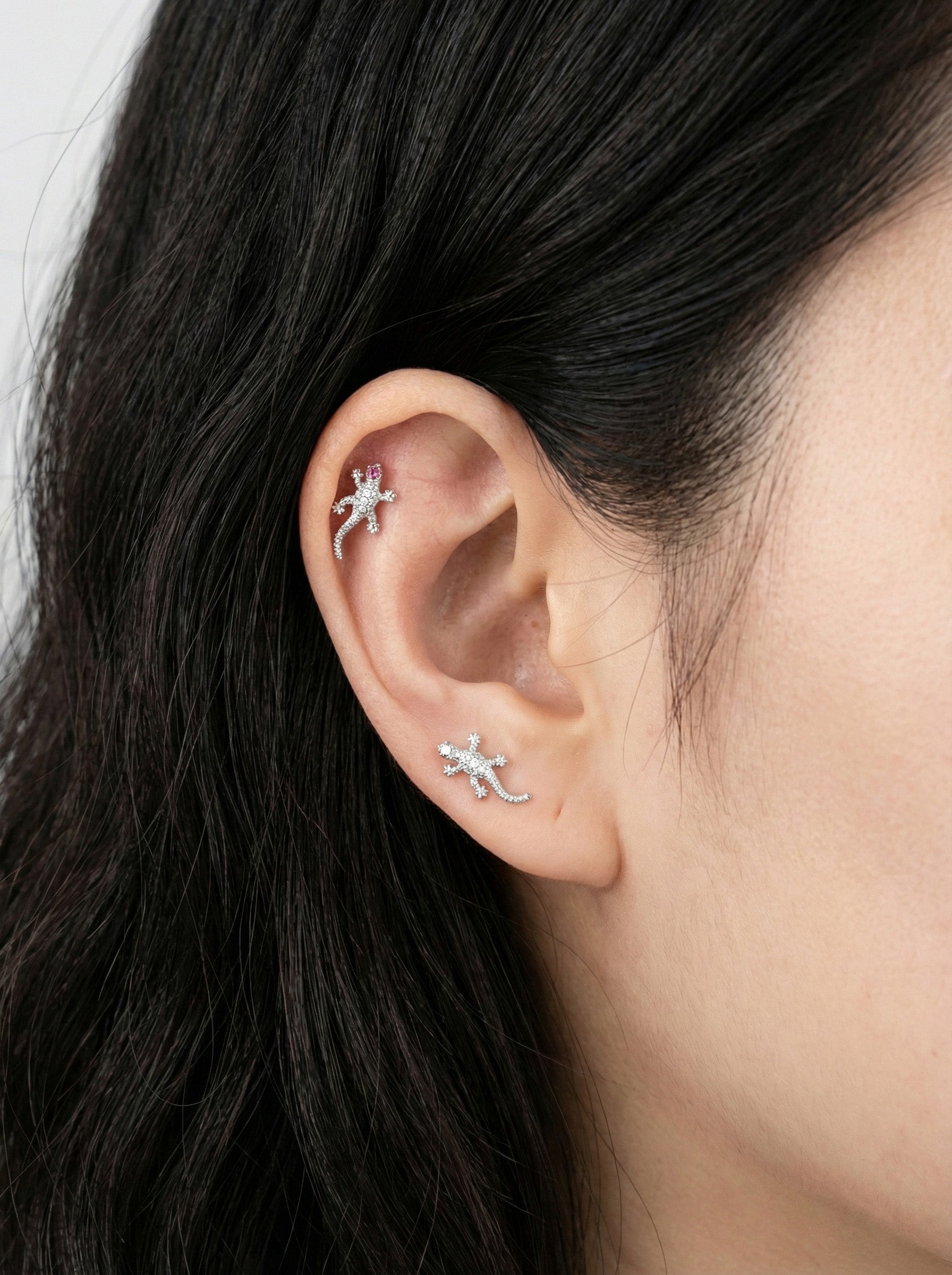 Close-up of an ear with two small lizard-shaped earrings.