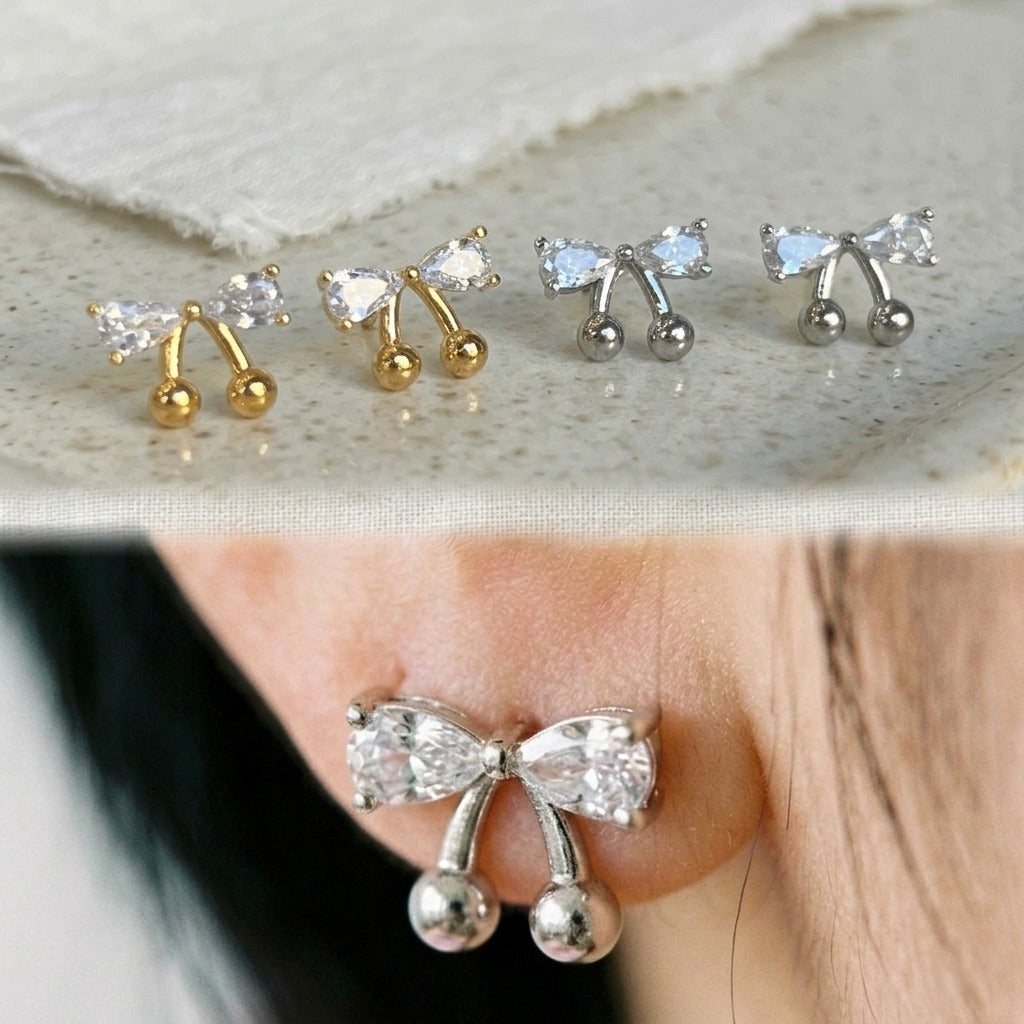 Collage showing gold and silver CZ bow cherry studs flat lay on top, and silver version worn on ear close-up on bottom, demonstrating both colorways and actual wear size