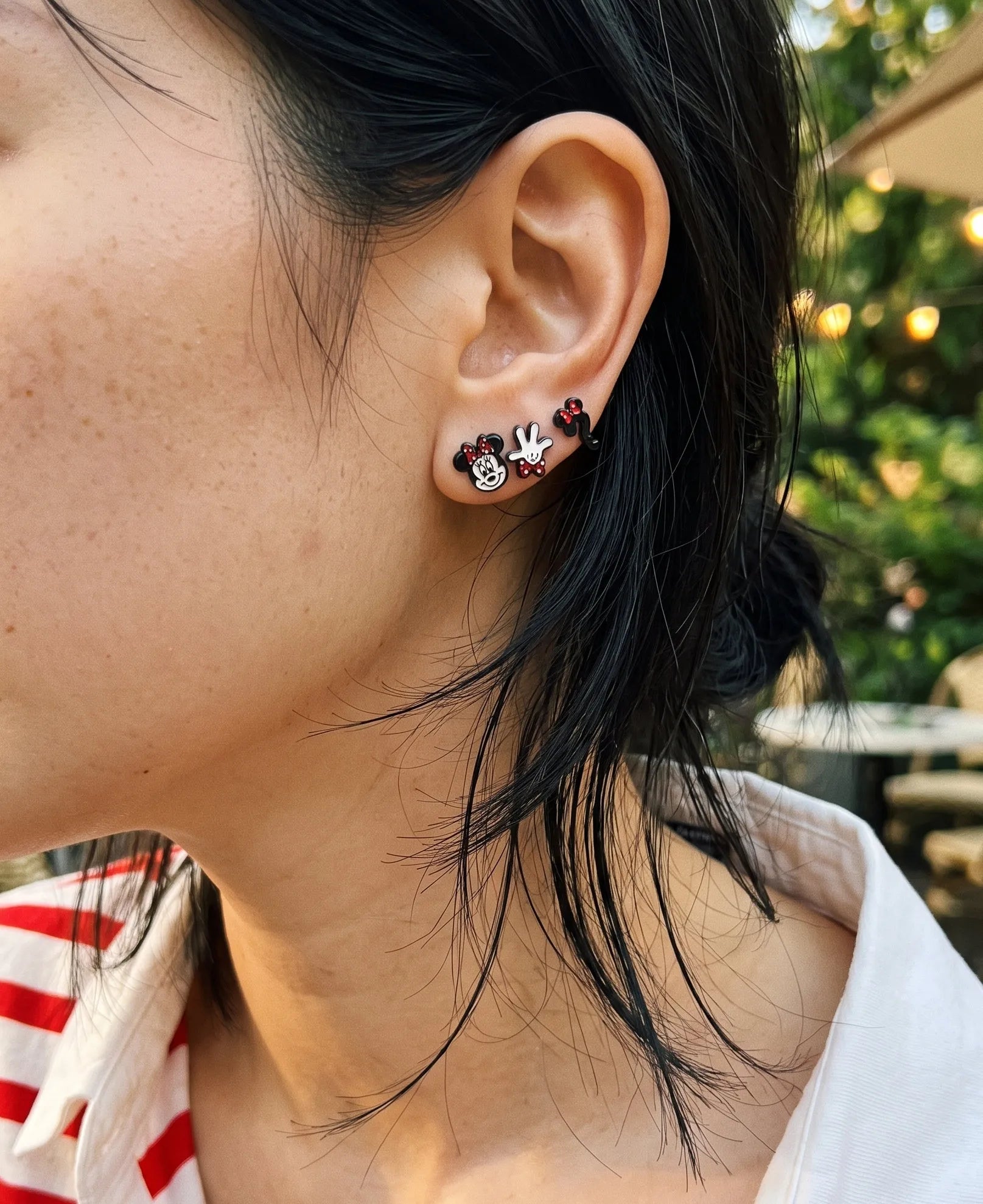 Close-up curated ear stack with mouse face, glove, and question mark enamel studs, K-style earring look