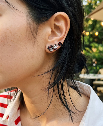 Close-up curated ear stack with mouse face, glove, and question mark enamel studs, K-style earring look