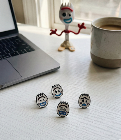 Four handmade Forky earrings displayed on white desk with laptop and coffee mug showing shocked winking happy sad faces