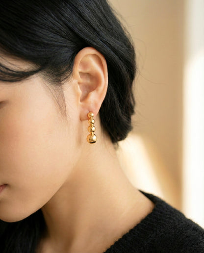 Close-up of gold 4-tier sphere stick earrings showing linear drop design