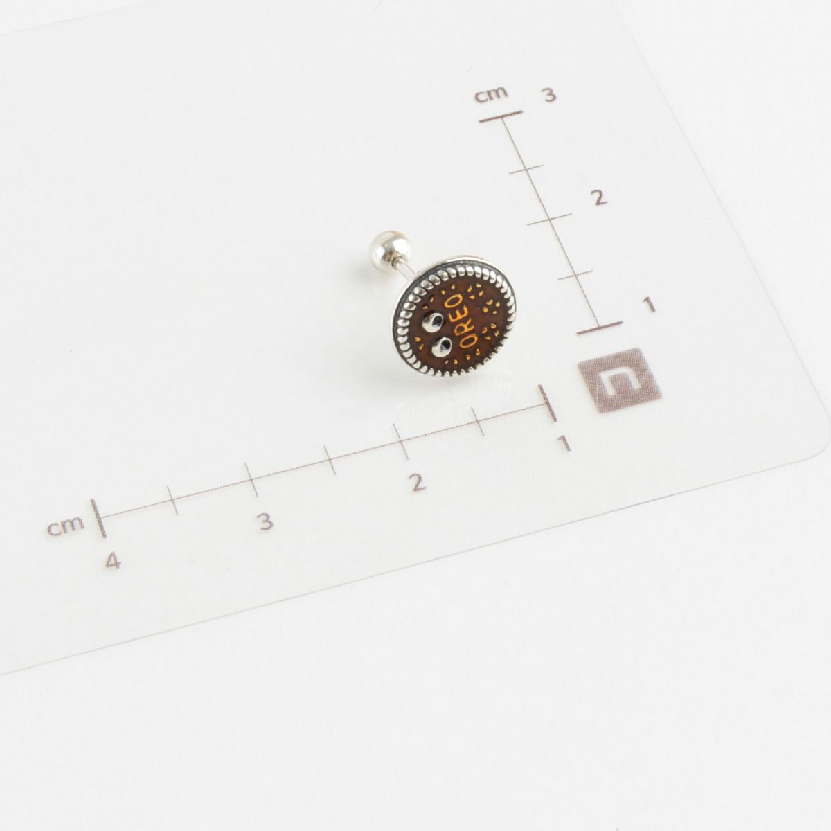 Size measurement of brown Oreo piercing with ruler showing approximately 8mm diameter