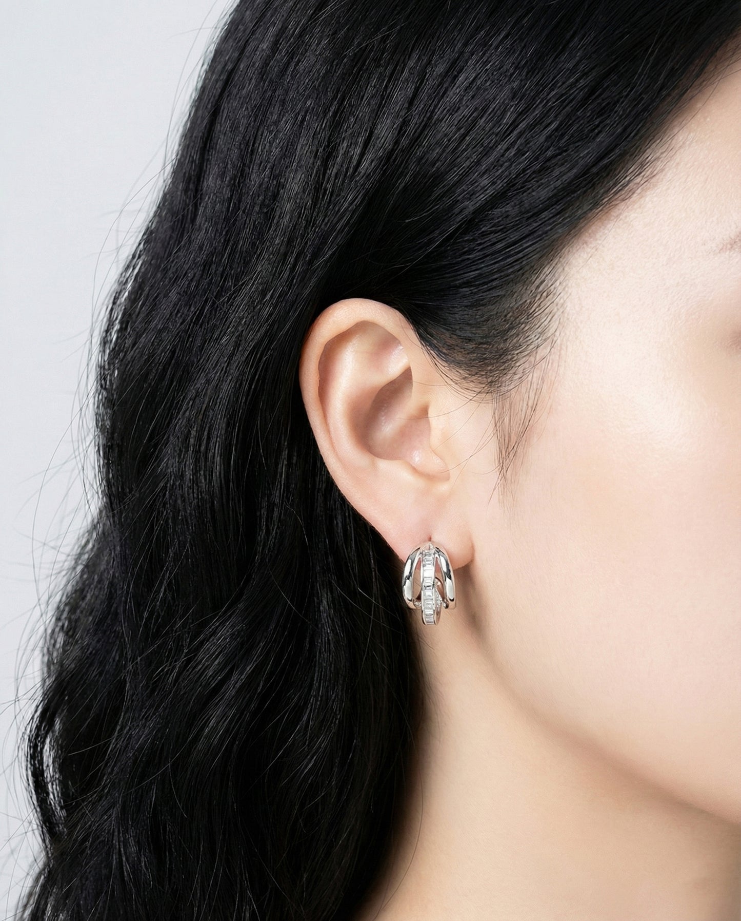 Silver triple row huggie earrings worn with dark hair and minimalist style